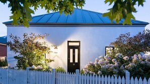 En hvid bygning med blå tag, en sort dør og et hvidt stakitterhegn.
