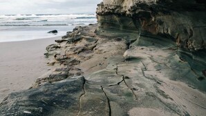 Eine Küstenlandschaft mit einer markanten Felsformation und einem Sandstrand.