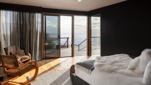 Ein Schlafzimmer mit einem großen Bett, einem Sessel, einem Deckenventilator und Meerblick durch eine Glasschiebetür.
