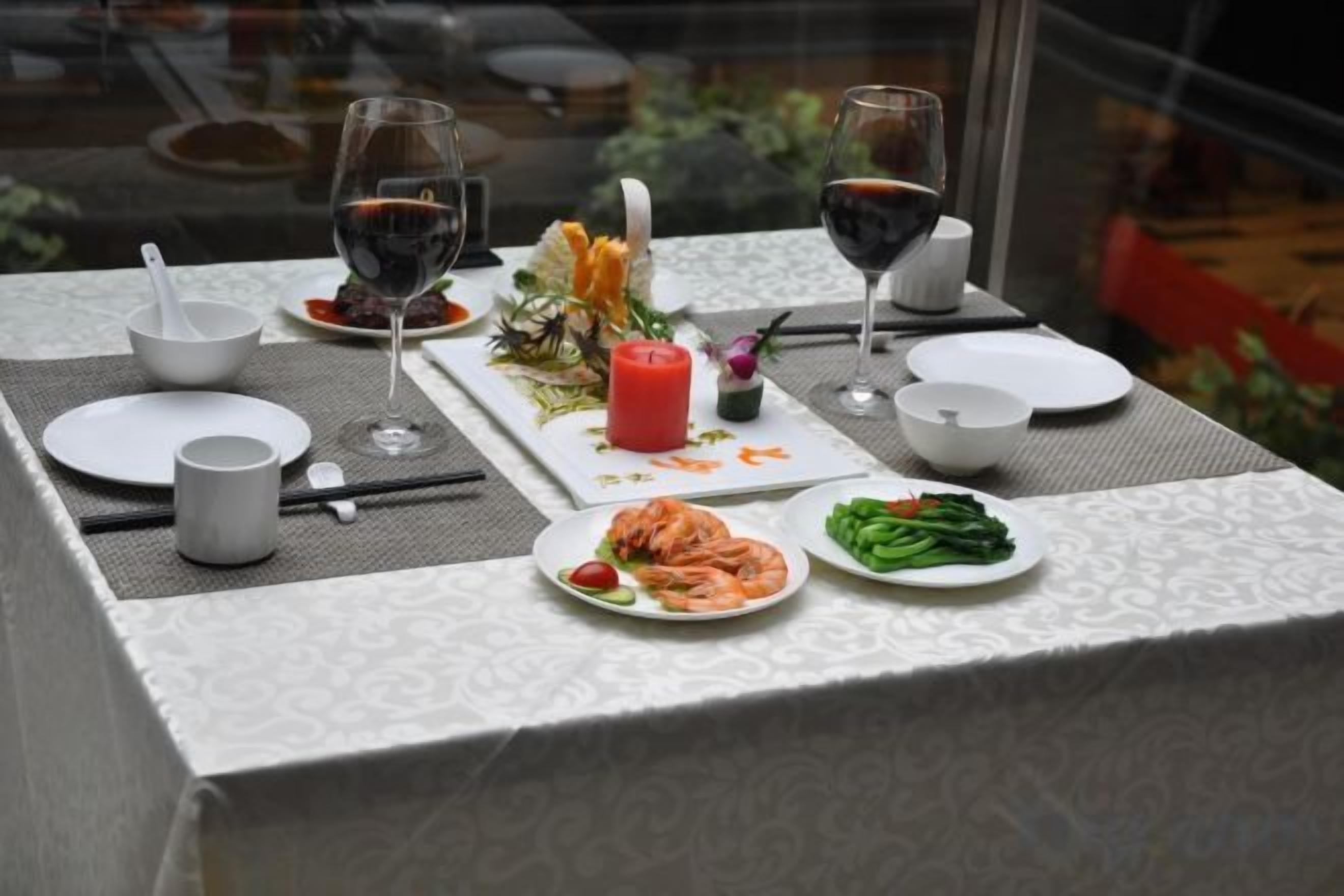 Una mesa dispuesta con platos, vasos y una vela, que sugiere un montaje para cenar.