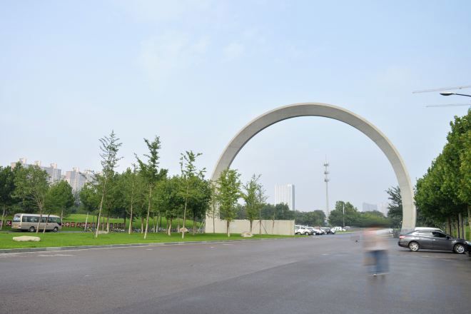 A road with a large arch structure, trees, and a clear sky.