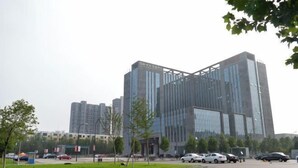 A modern building with a glass facade and a parking lot in front.