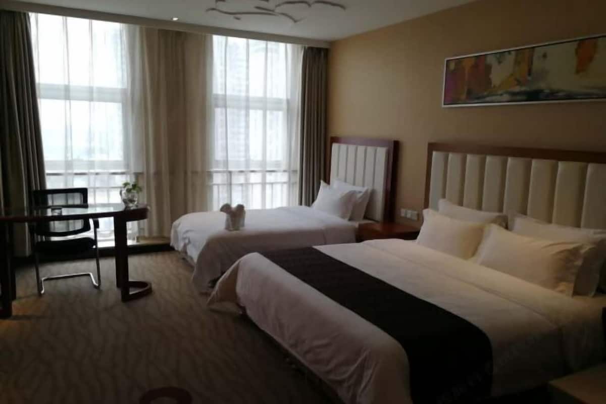 Ein Hotelzimmer mit zwei Betten, einem Schreibtisch und einem großen Fenster mit Vorhängen.