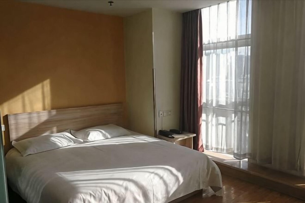 A hotel room with a bed, bedside table, and a window with curtains.