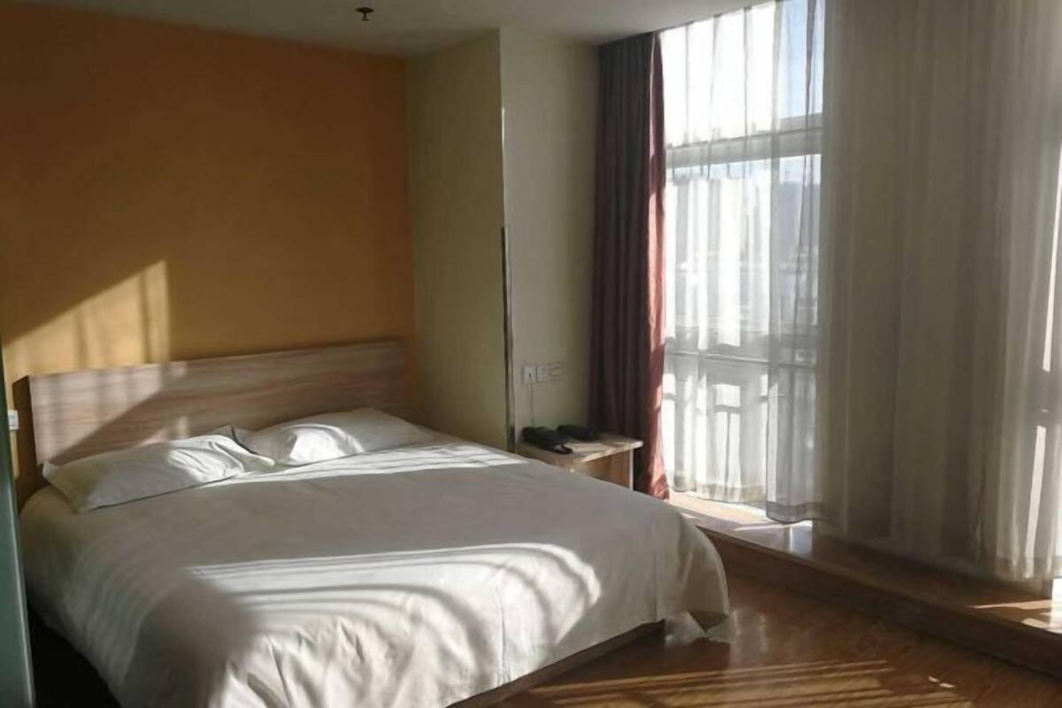 Ein Hotelzimmer mit einem großen Bett, einem Nachttisch und einem Fenster mit Vorhängen.