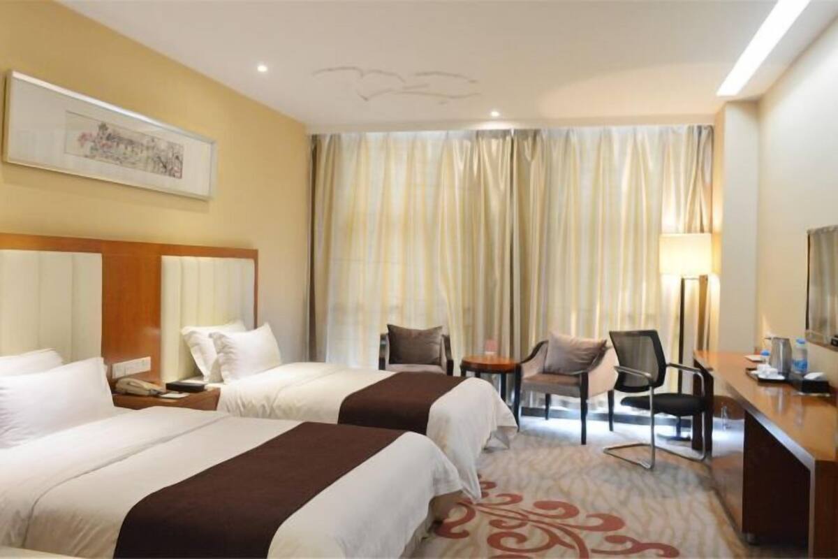 Ein Hotelzimmer mit zwei Betten, einem Schreibtisch, einem Stuhl, einer Lampe und einem Vorhang.