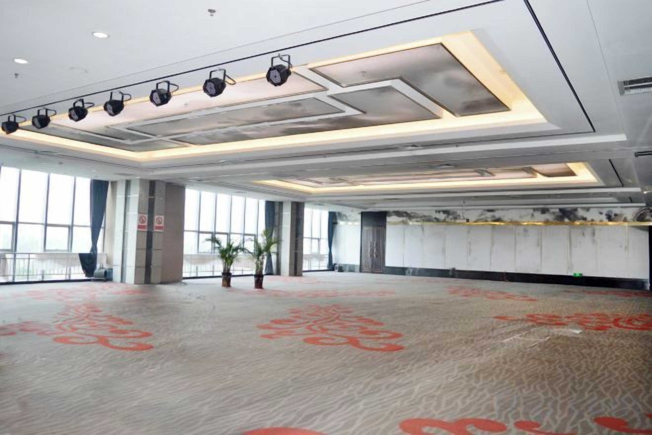 A large, open indoor space with a patterned floor, a high ceiling with recessed lighting, and large windows.