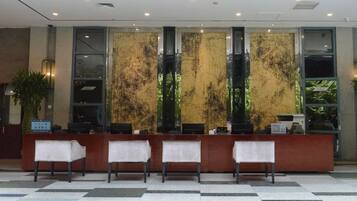 A reception desk with three chairs, a check-in counter, and a large window with a view of greenery.