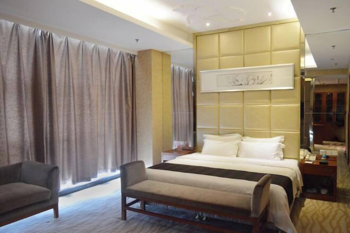 Ein Hotelzimmer mit einem großen Bett, einer Couch, einem Nachttisch und einem großen Fenster mit Vorhängen.