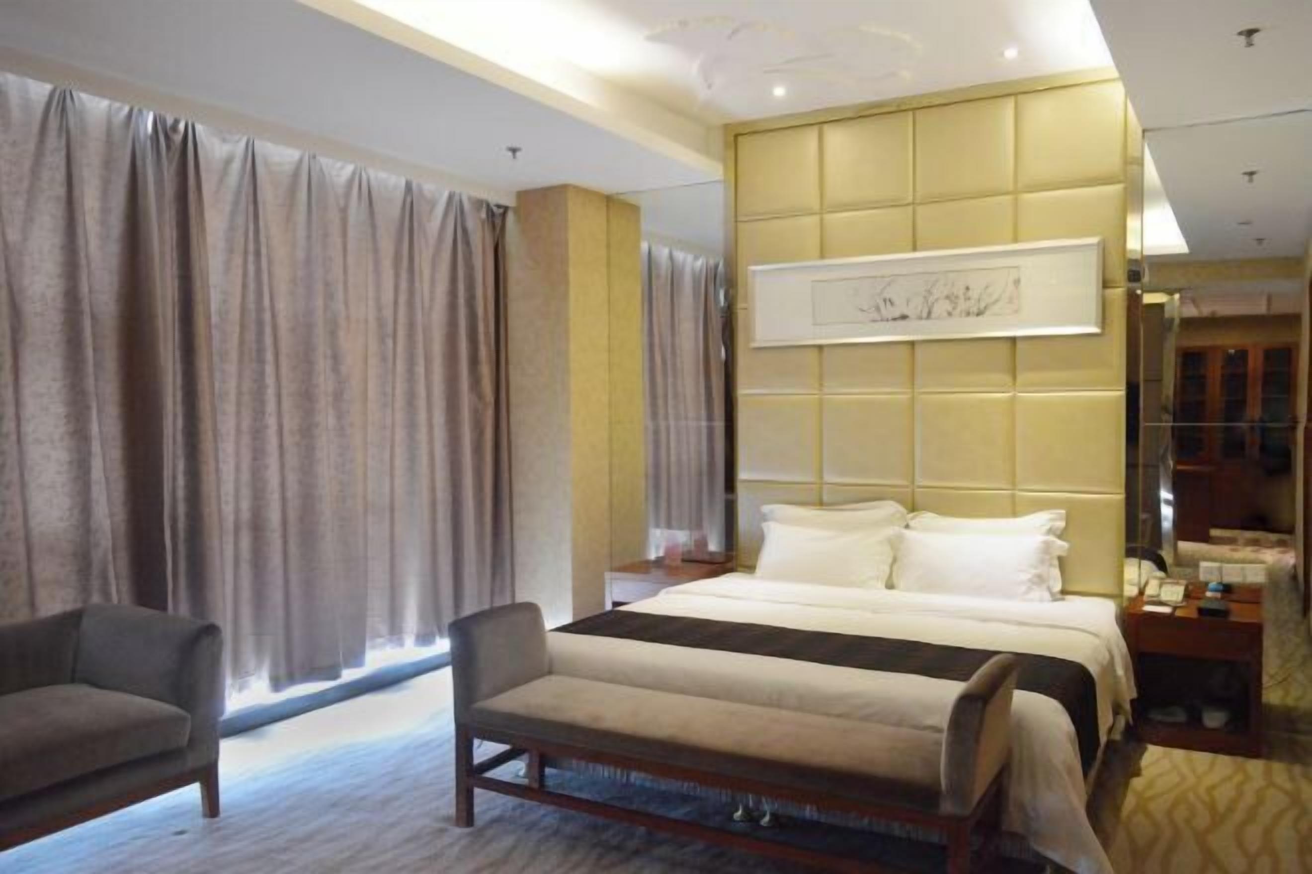 Una habitación de hotel con cama, una silla, una mesita de noche y un ventanal con cortinas.
