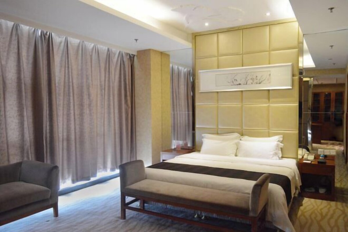 Una habitación de hotel con cama, una silla, una mesita de noche y un ventanal con cortinas.