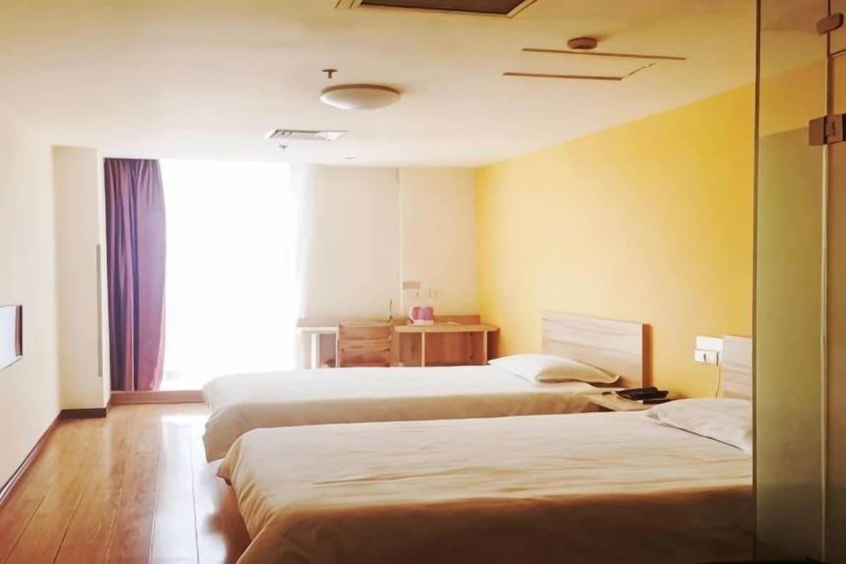 A hotel room with two beds, a bedside table, a nightstand, and a window with curtains.