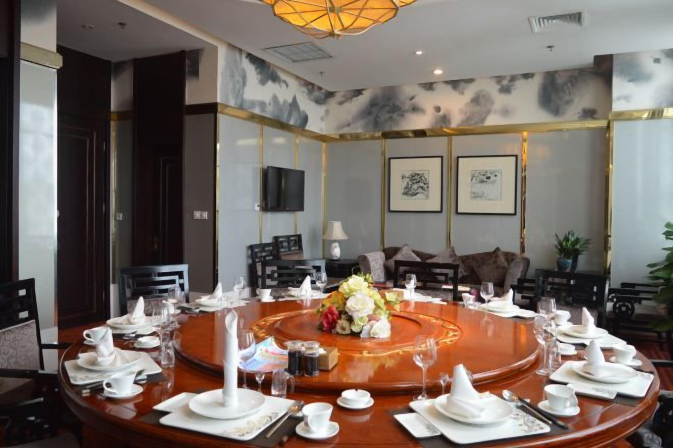 A conference room with a round table set for a meeting, equipped with chairs, a television, and framed artwork on the walls.