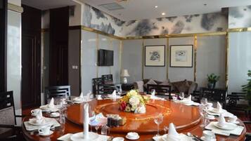 A conference room with a round table set for a meeting, equipped with chairs, a television, and framed artwork on the walls.