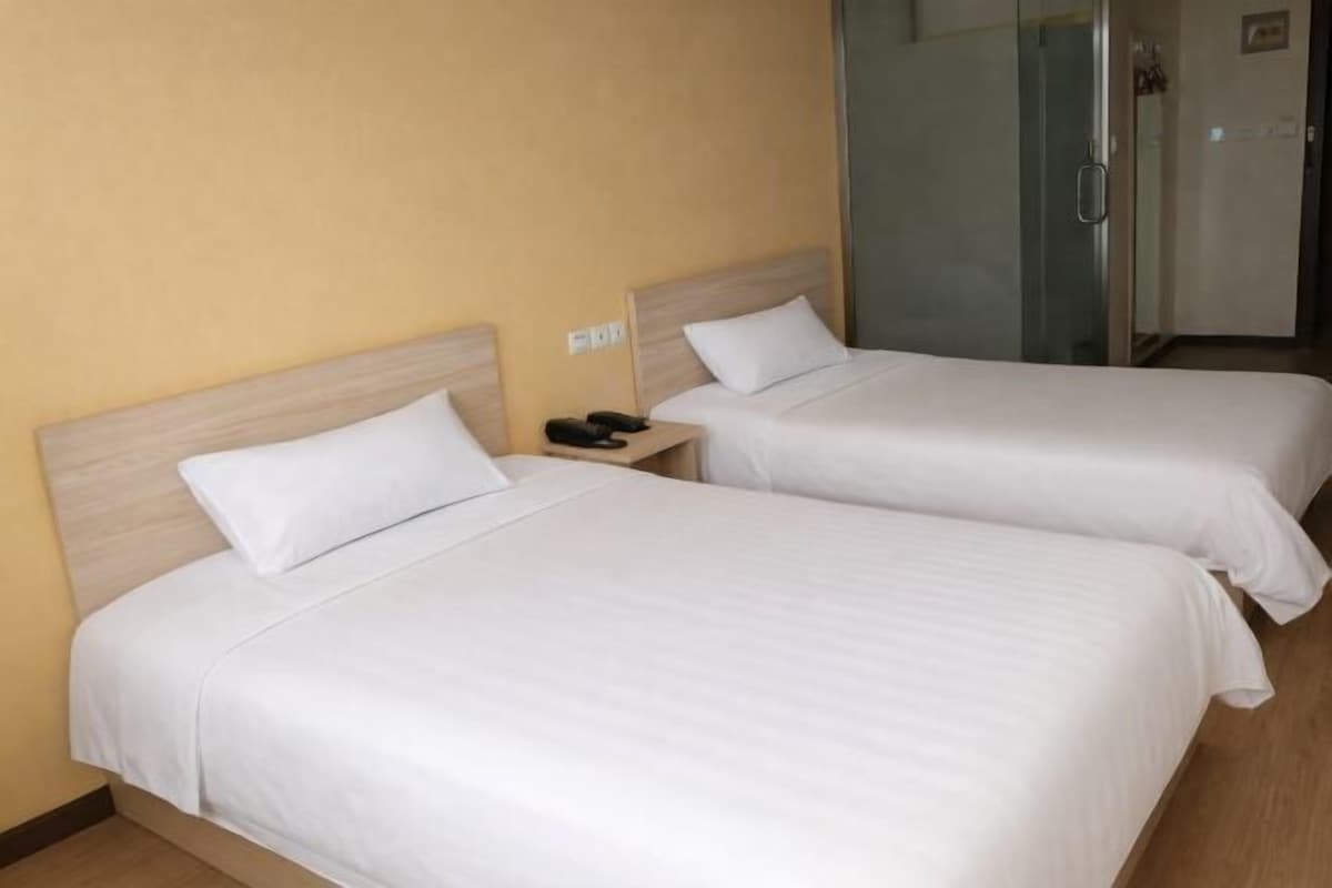 A hotel room with two beds, a bedside table with a phone, and a glass door leading to a bathroom.