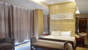 A hotel room with a bed, a chair, a bedside table, and a large window with curtains.