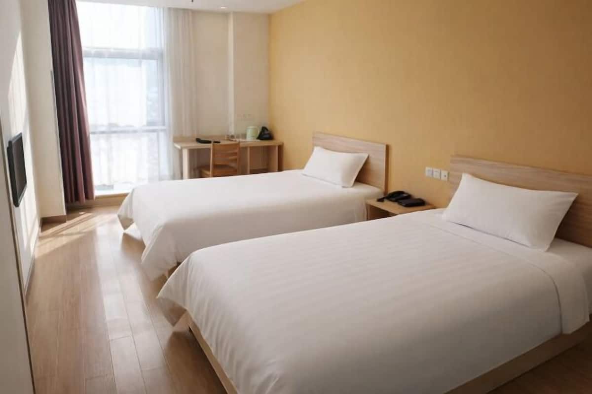 Ein Hotelzimmer mit zwei Betten, einem Schreibtisch und einem fenster mit Vorhängen.