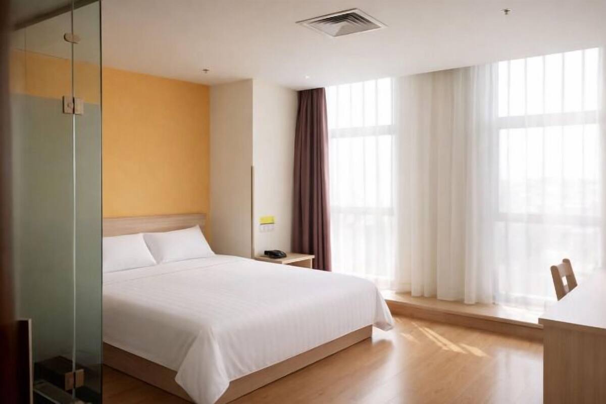 Ein Hotelzimmer mit Bett, Nachttisch, Spiegel und einem Fenster mit Vorhängen.