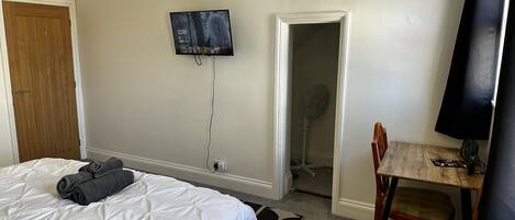 A bedroom with a bed, a TV mounted on the wall, a wooden door, and a chair with a table.