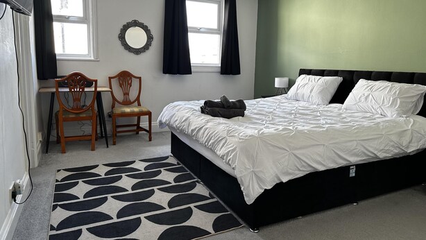 A bedroom with a bed, two chairs, a desk, a lamp, and a window with curtains. - Family Friendly One Bedroom Apartment w King Bed (Colchester)