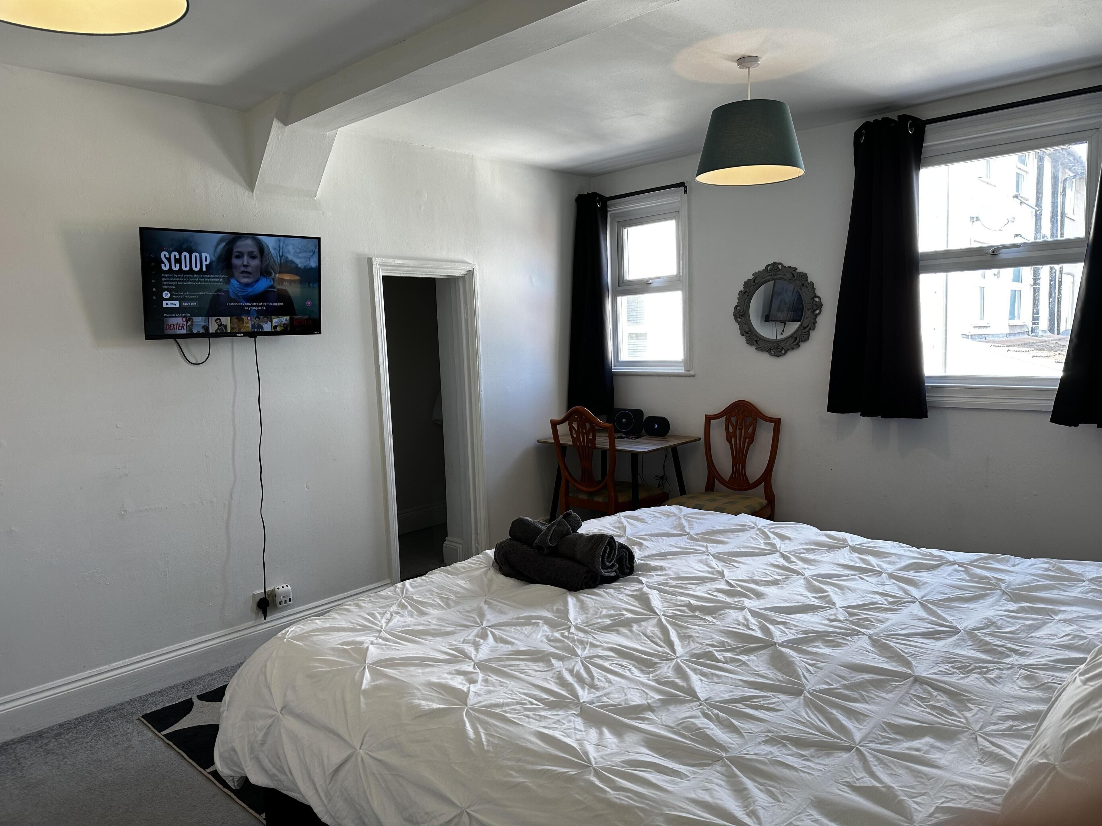 Un dormitorio con cama, un escritorio con silla, un televisor y una ventana con cortinas.