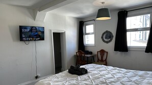 A bedroom with a bed, a desk with a chair, a television, and a window with curtains. - Family Friendly One Bedroom Apartment w King Bed (Colchester)