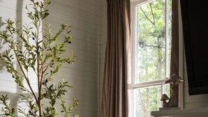 Una habitación acogedora con un banco de madera, una lámpara y una planta en maceta junto a una ventana con cortinas.