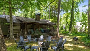 A rustic cabin with a porch, surrounded by trees. There is a fire pit with chairs and a grill nearby. - The Cabin - Fire Pit, Pool Table, Spacious (Greensboro)