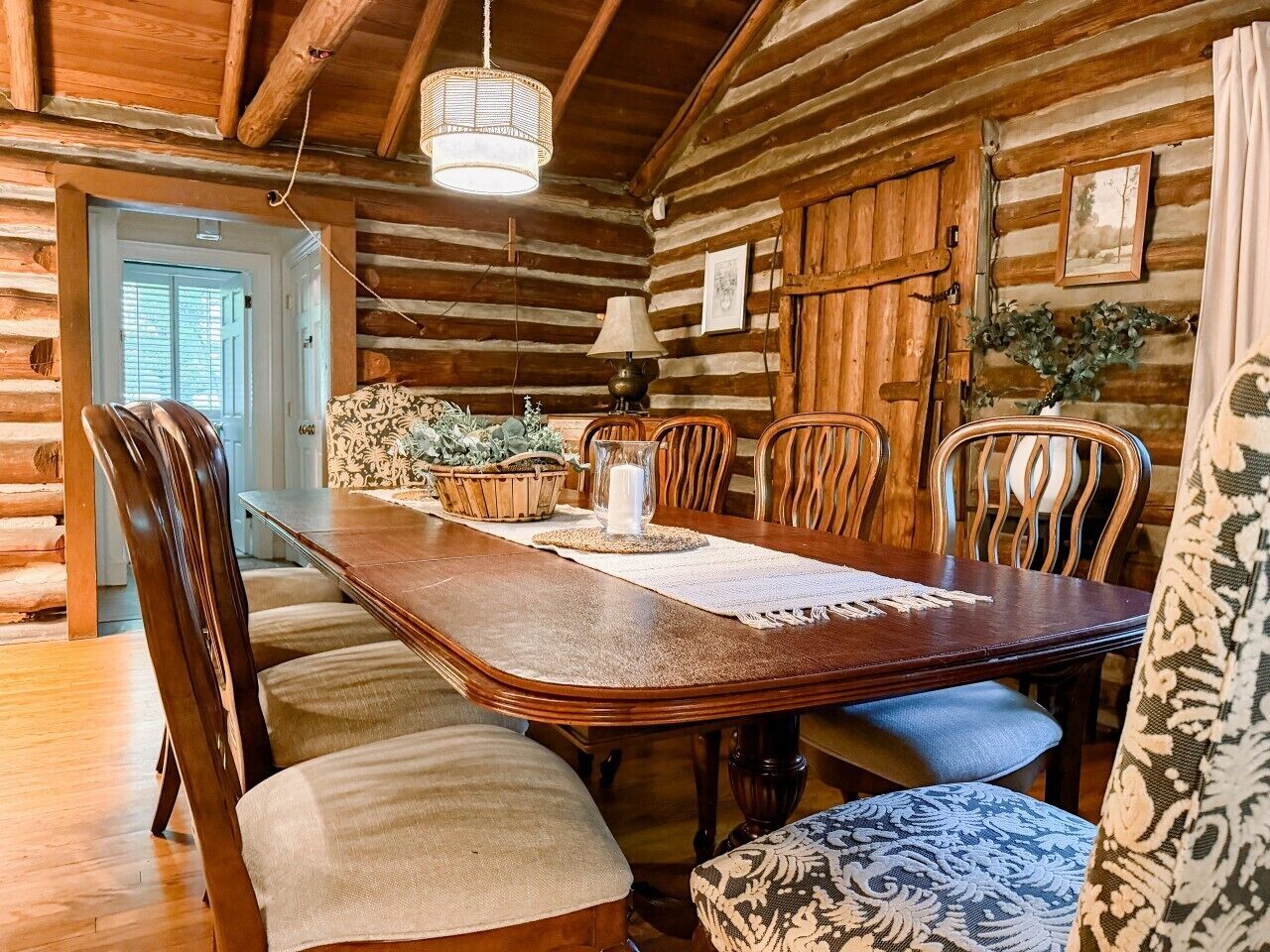 A wooden log cabin interior with a dining table, chairs, and a hanging light fixture.
