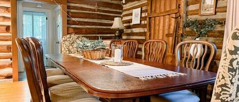 A wooden log cabin interior with a dining table, chairs, and a hanging light fixture.