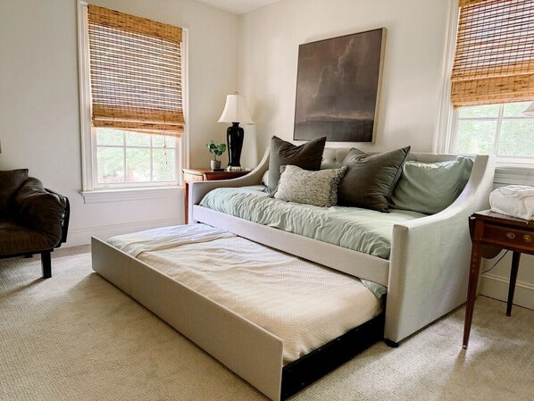 Un dormitorio con cama, mesita de noche, lámpara y un amplio ventanal con persianas.