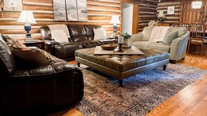 A log cabin interior with leather sofas, a patterned rug, and wooden walls. - The Cabin - Fire Pit, Pool Table, Spacious (Greensboro)