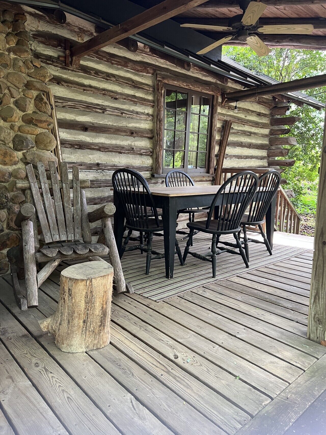 Un rustico chalet in legno con un tavolo rotondo e quattro sedie, una parete in pietra e un portico in legno.