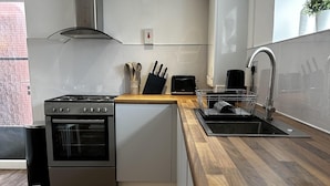A modern kitchen with a built-in oven, a stainless steel range hood, a sink, and a wooden countertop. - Entire Apartment Super King Bed Close To Town (Colchester)