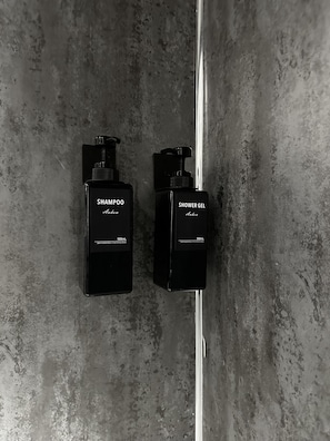 Twee zwarte flessen Anahom shampoo en douchegel, elk met de aanduiding 500mL, staan op een gestructureerde grijze muur.