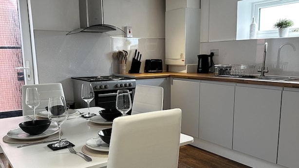 A modern kitchen with white cabinets, a gas stove, and a dining area with a white table and chairs. - Entire Apartment Super King Bed Close To Town (Colchester)
