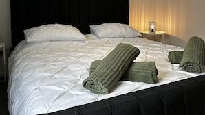 A neatly made bed with white linens and green towels, a black headboard, and a framed picture on the wall. - Entire Apartment Super King Bed Close To Town (Colchester)