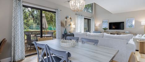Uma sala de estar moderna com área de jantar, um candelabro e uma televisão.