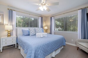 A bedroom with a bed, two bedside tables, a ceiling fan, and windows with blinds.