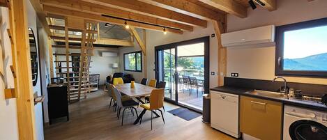 A modern kitchen with a dishwasher, a dining area with a table and chairs, a staircase, and a view of the outdoors.