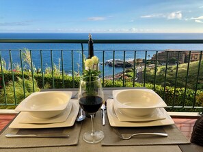 A table set for two with a glass of red wine and a vase of flowers, overlooking a coastal view. - Oceanic Apartments  (Santa Cruz)