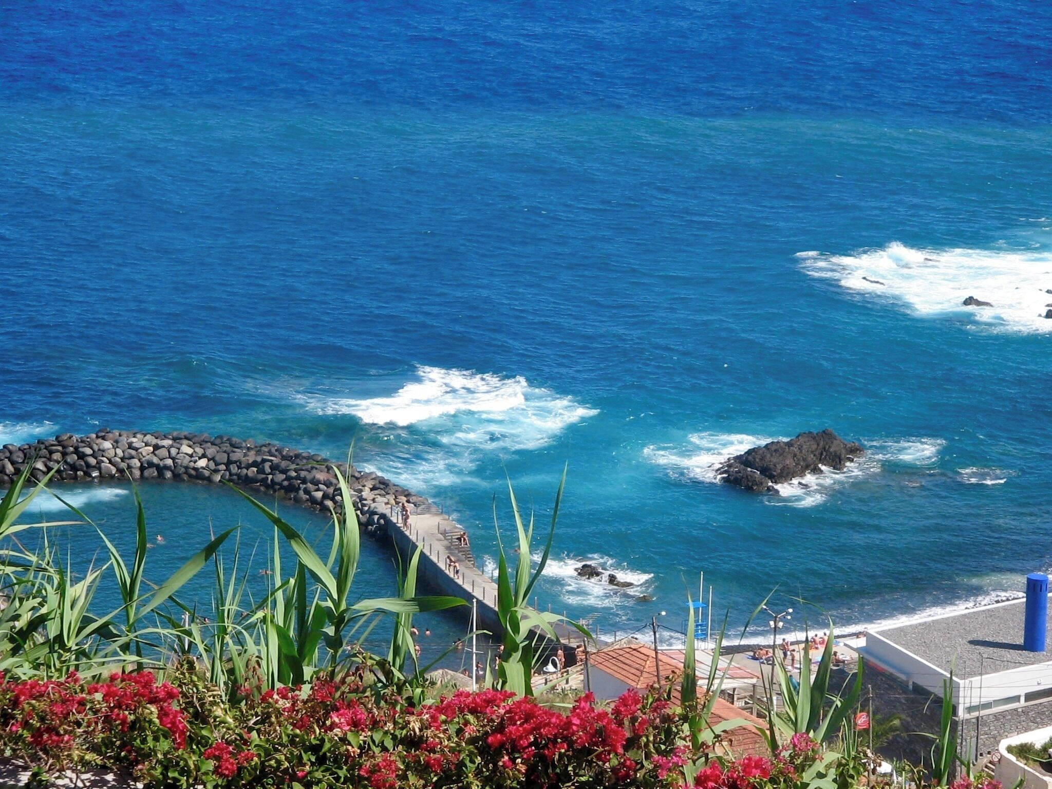 A coastal view with a rocky breakwater, a swimming area, and a building with a red roof.