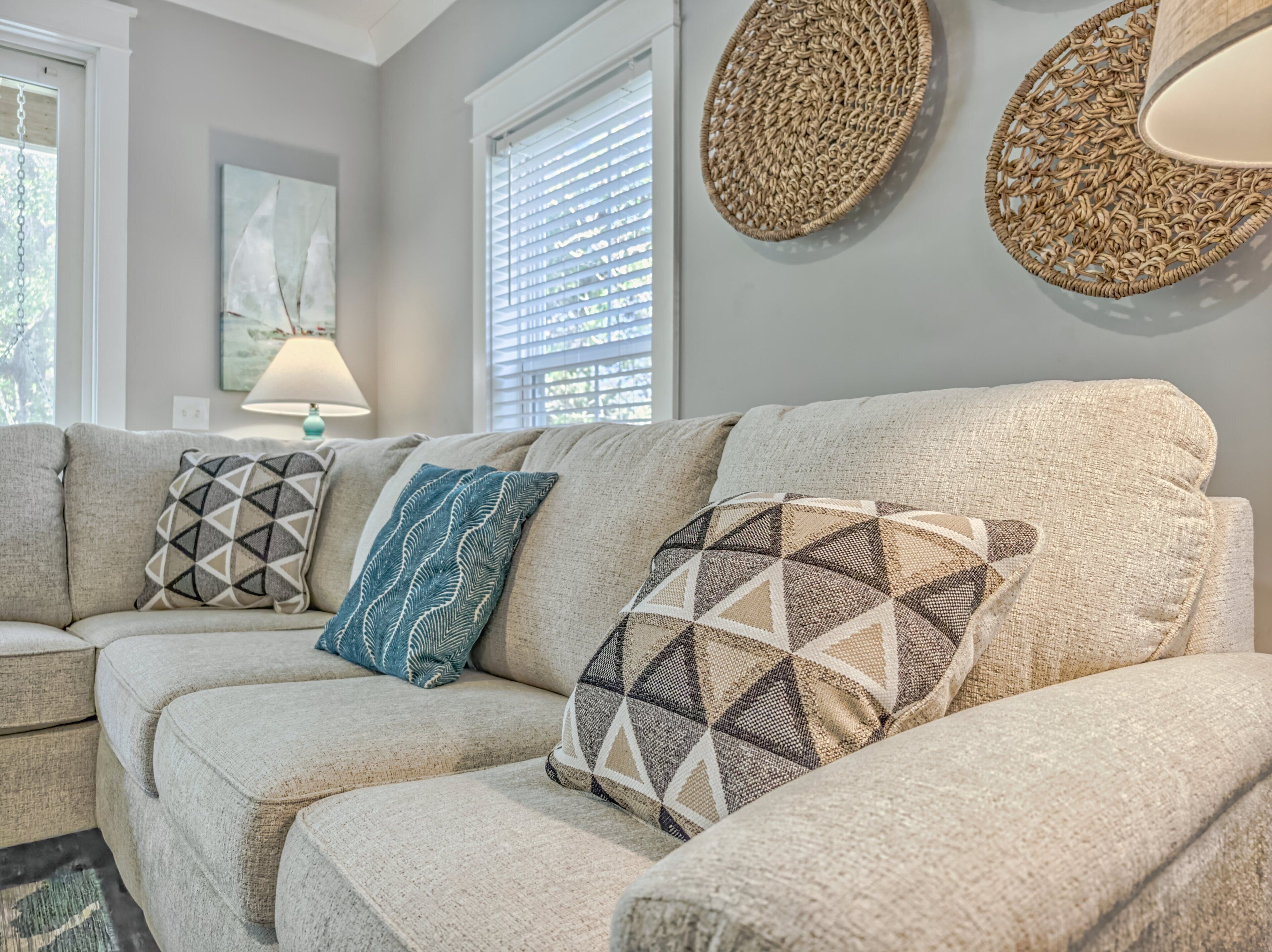 A sectional sofa with patterned cushions, a woven wall hanging, and a lamp on a side table.