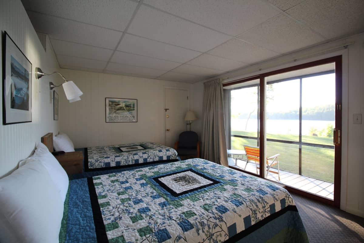 A hotel room with two beds, a large window, and a view of a grassy area.