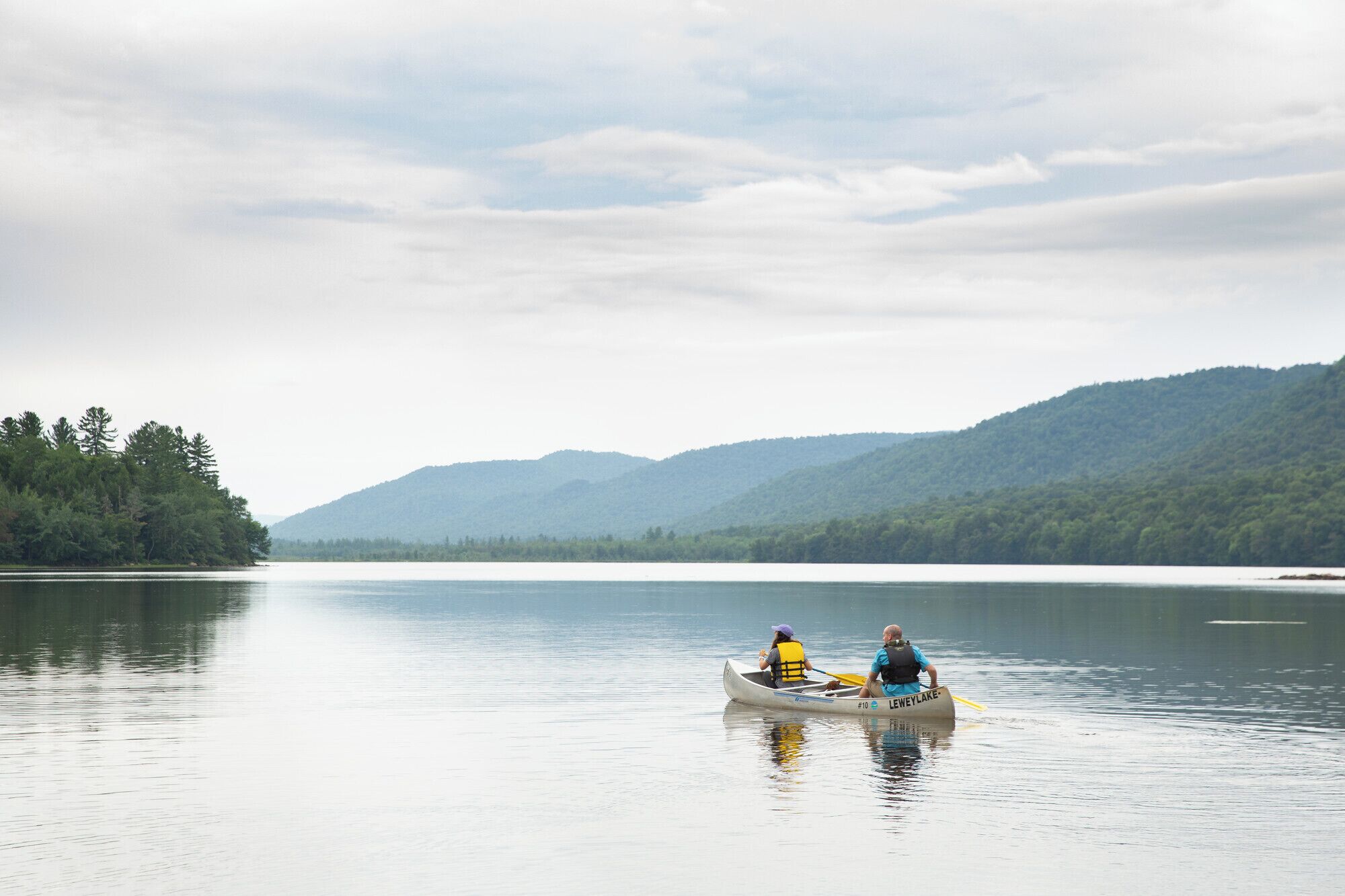 A calm lake with two people in a canoe, surrounded by forested hills.