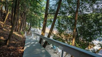 A wooden pathway leading to a beach with a railing, surrounded by trees.