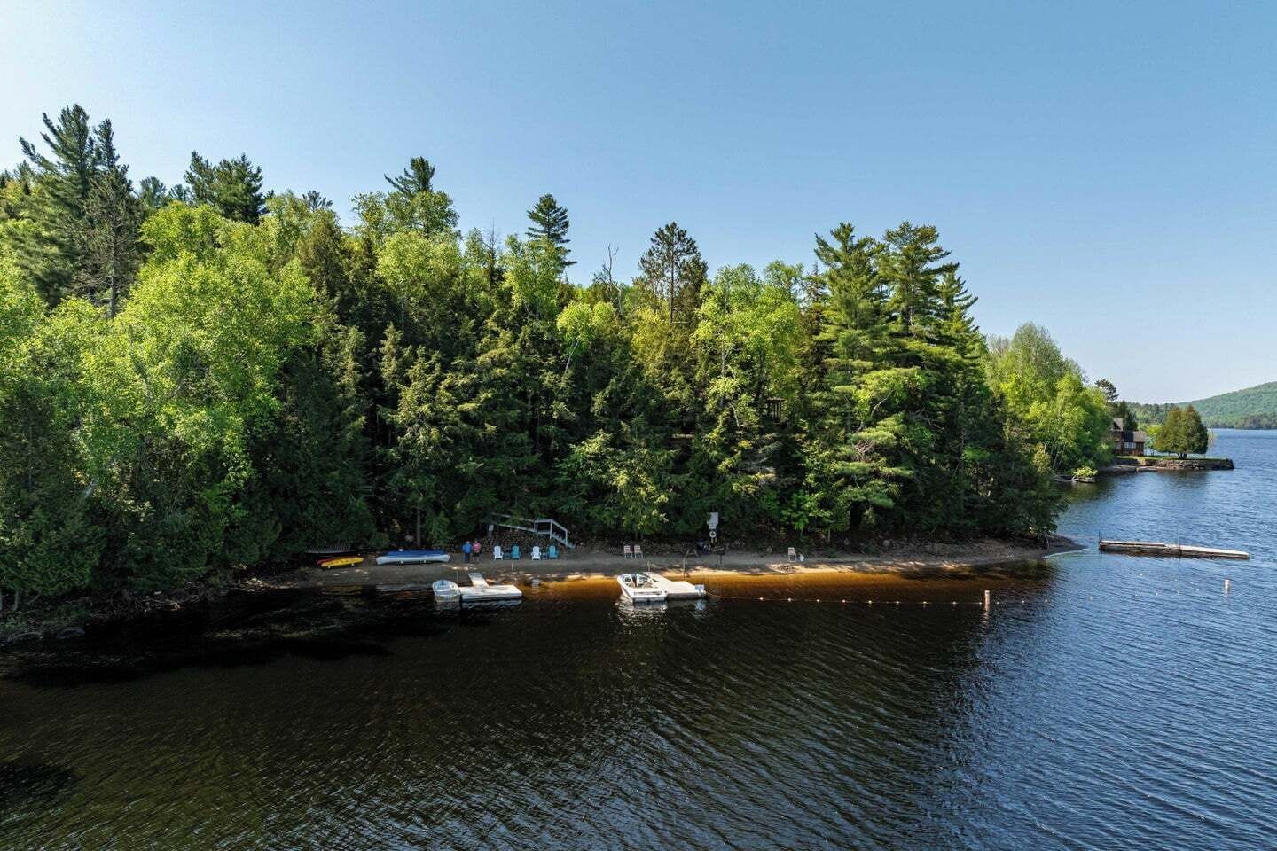 Una cabaña junto al lago con barcos amarrados, rodeada de un bosque frondoso.