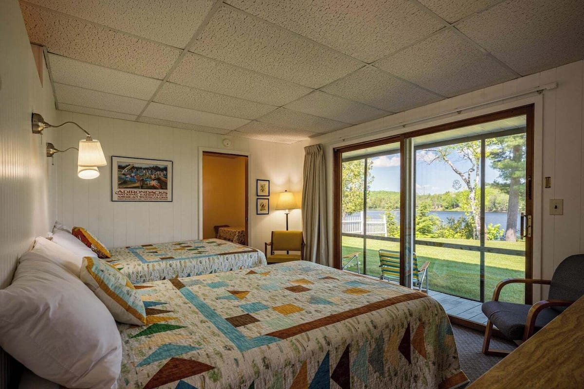 A hotel room with two beds, a large window with a view of a lake, and a chair by the window.