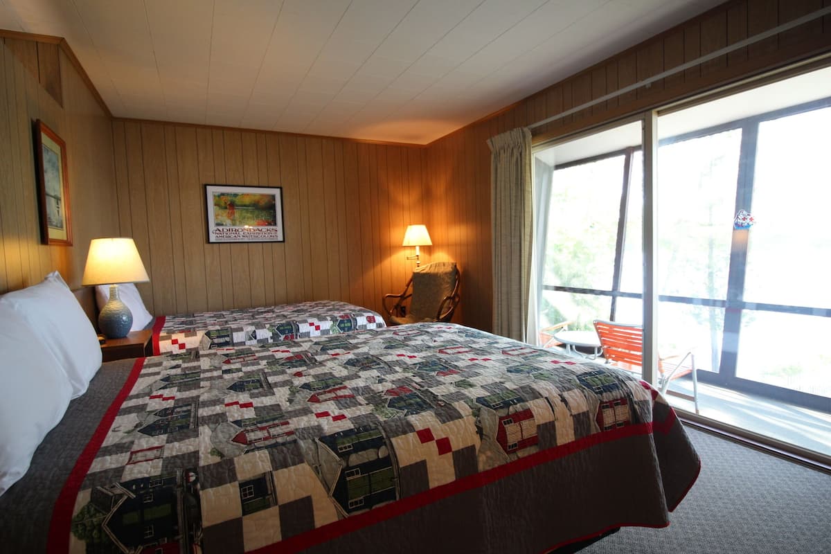 A hotel room with a large bed, two bedside lamps, a chair, a window with curtains, and a framed picture on the wall.
