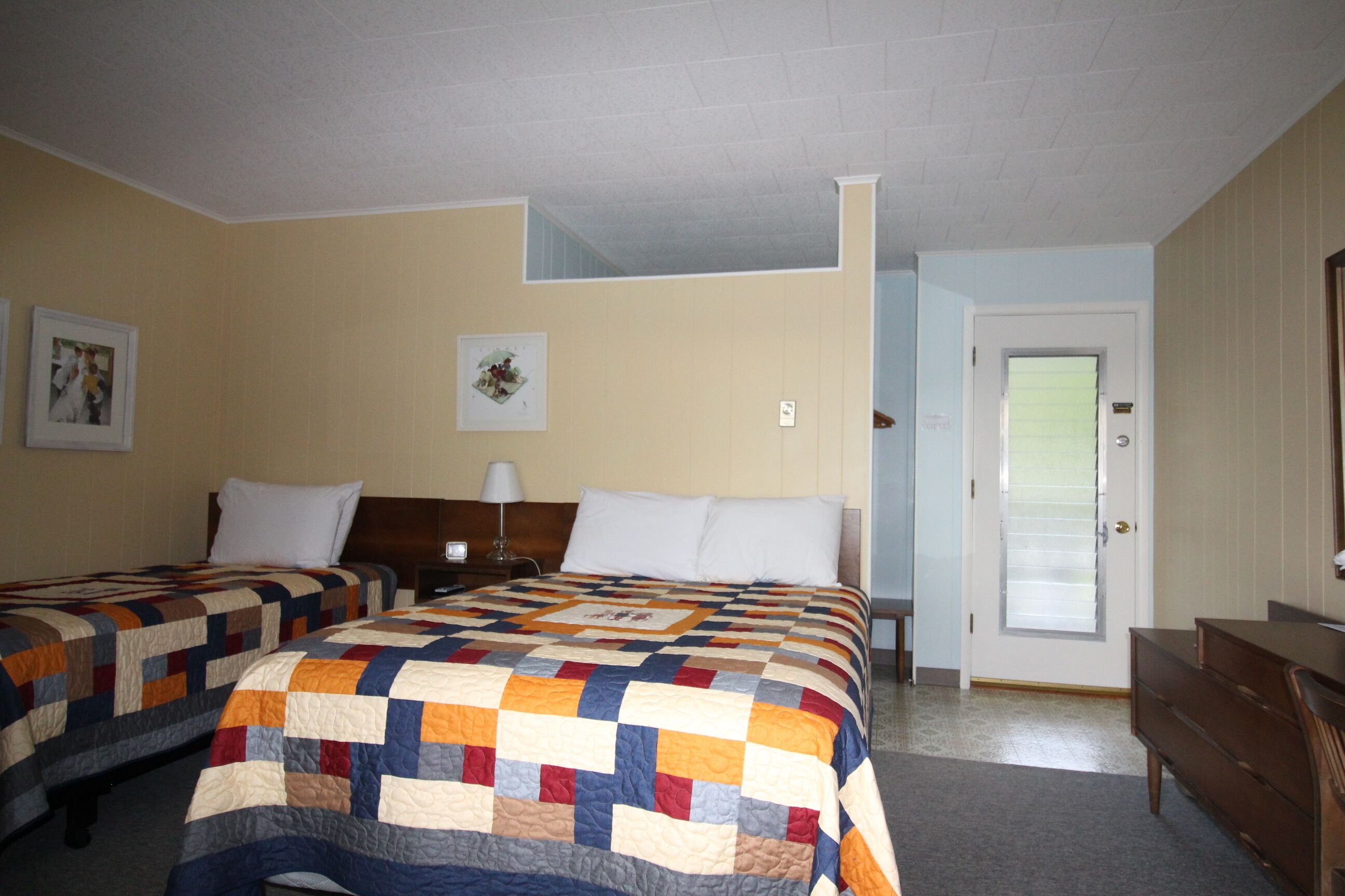 Une chambre d’hôtel avec deux lits, un bureau et une porte.